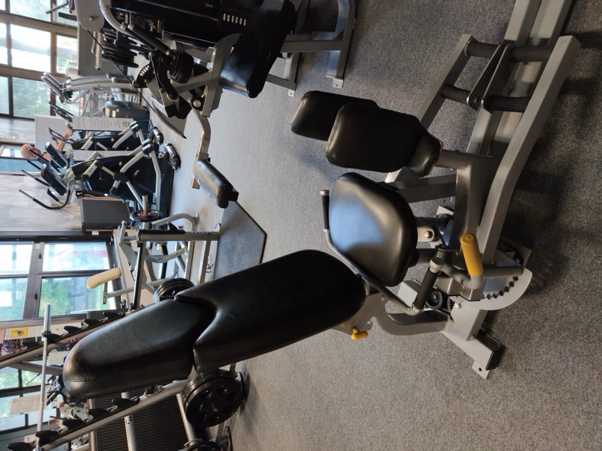 A hip abductor machine with knee pads and range-of-motion selector in a gym