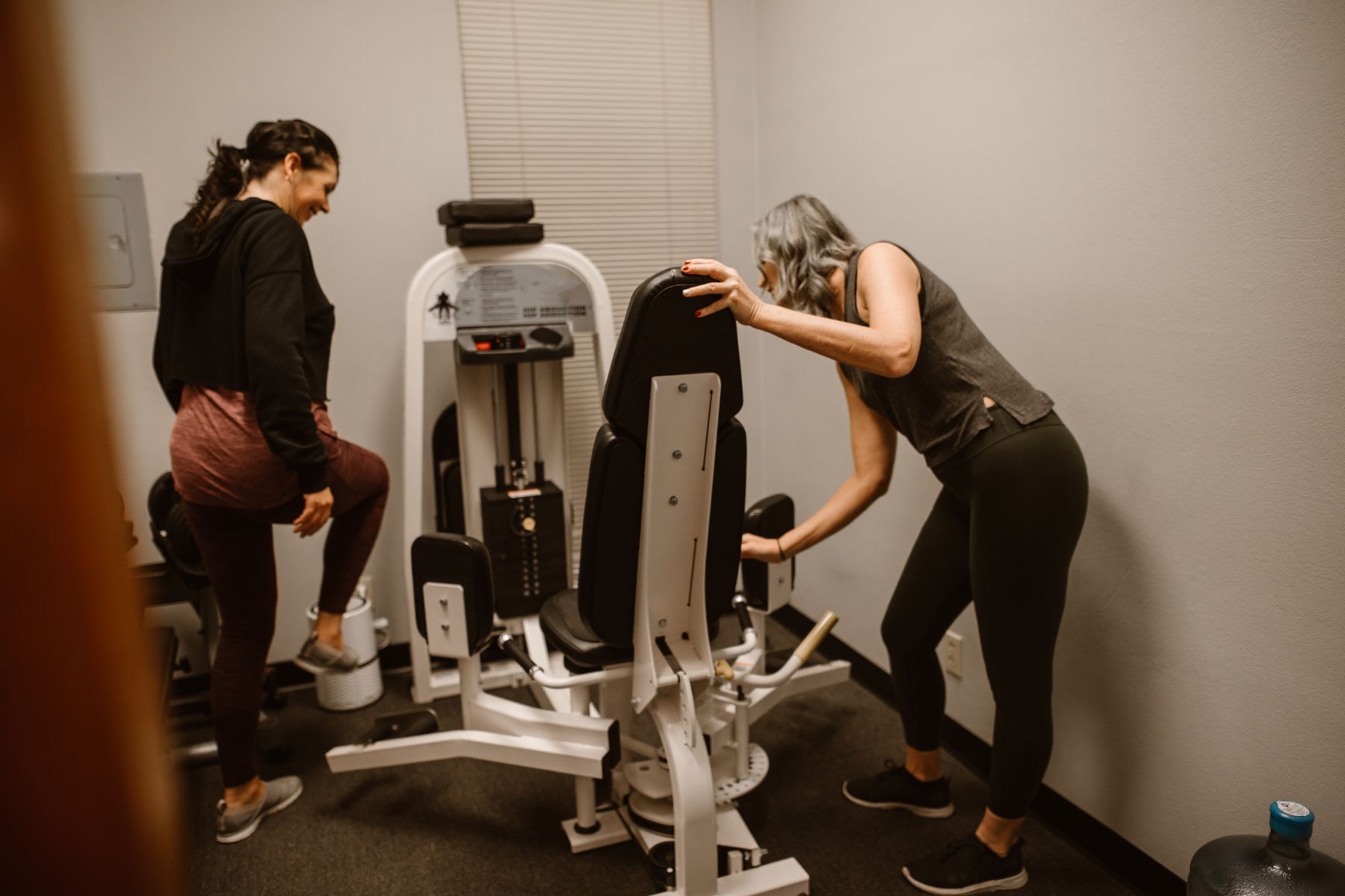 A trainer adjusts the setup of a hip abduction machine for a client